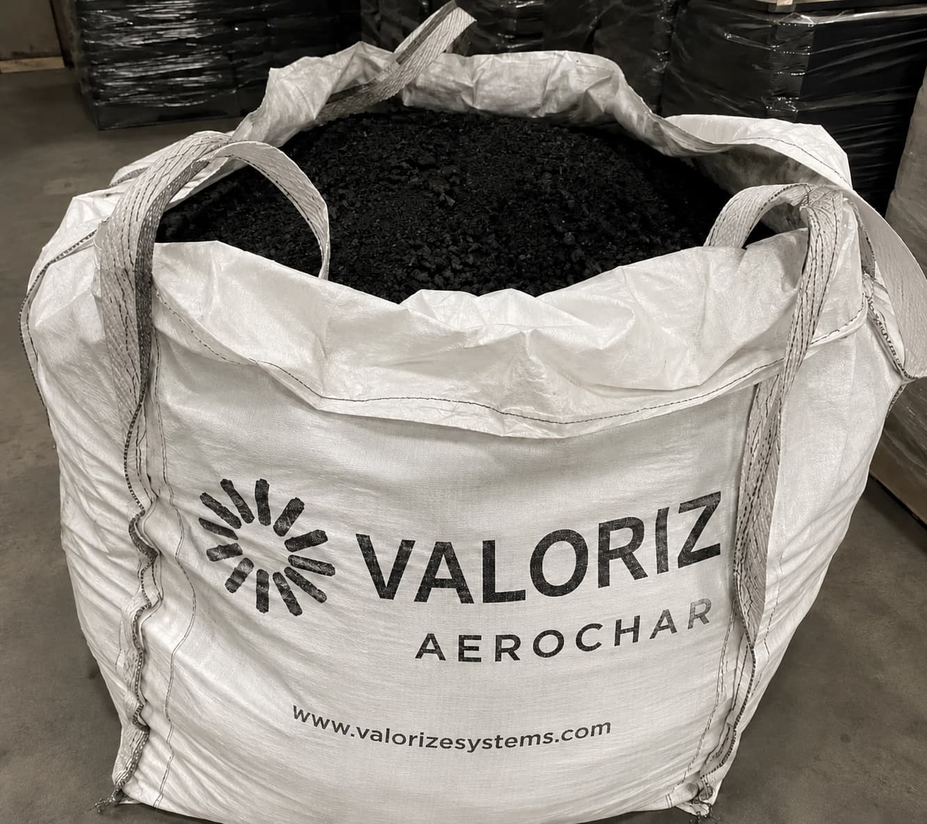 A branded Valorize AeroChar supersack, open at the top and filled with coarse black engineered biochar, on a warehouse floor.
